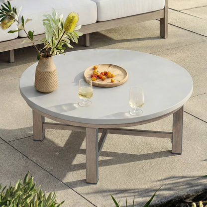 Round outdoor coffee table with a vase, fruit plate, and glasses on a patio.
