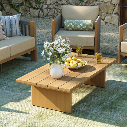 Elevated view of a minimalist faux-wood aluminum outdoor coffee table with solid block legs on a green textured patio rug.