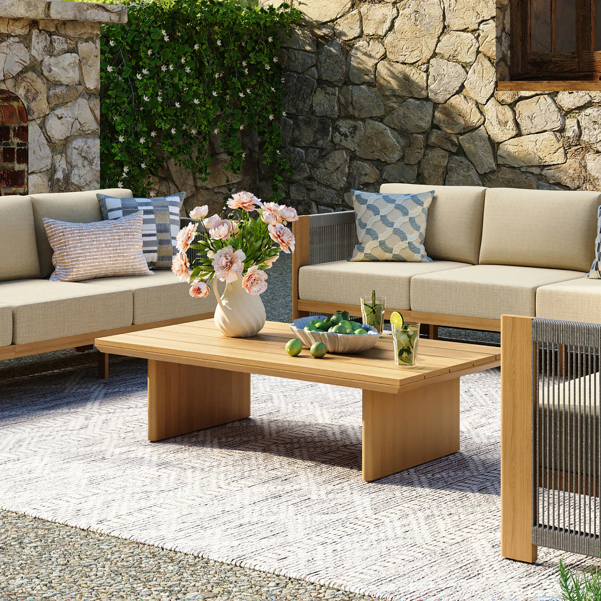 Rectangular wood grain aluminum coffee table styled with a white flower vase next to a beige outdoor sectional sofa on a patterned rug.