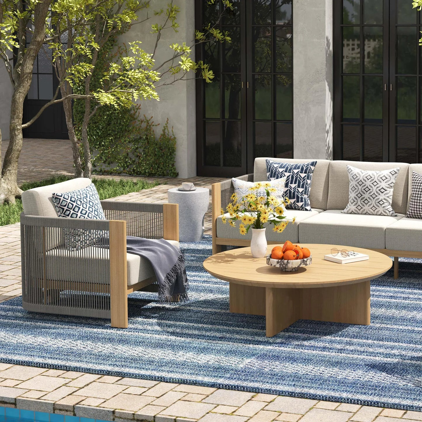 Outdoor patio setting with a sofa, chair, and coffee table on a blue striped rug.