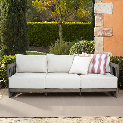 Outdoor patio sofa with light beige cushions and a gray metal frame, styled with two throw pillows in a garden setting.