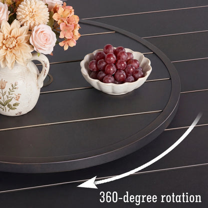 Round black tray with a bowl of grapes and a vase of flowers on a dark surface.