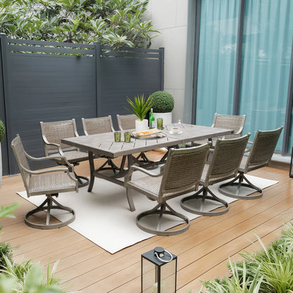 Outdoor dining set with table and chairs on a wooden deck, surrounded by plants and a building.