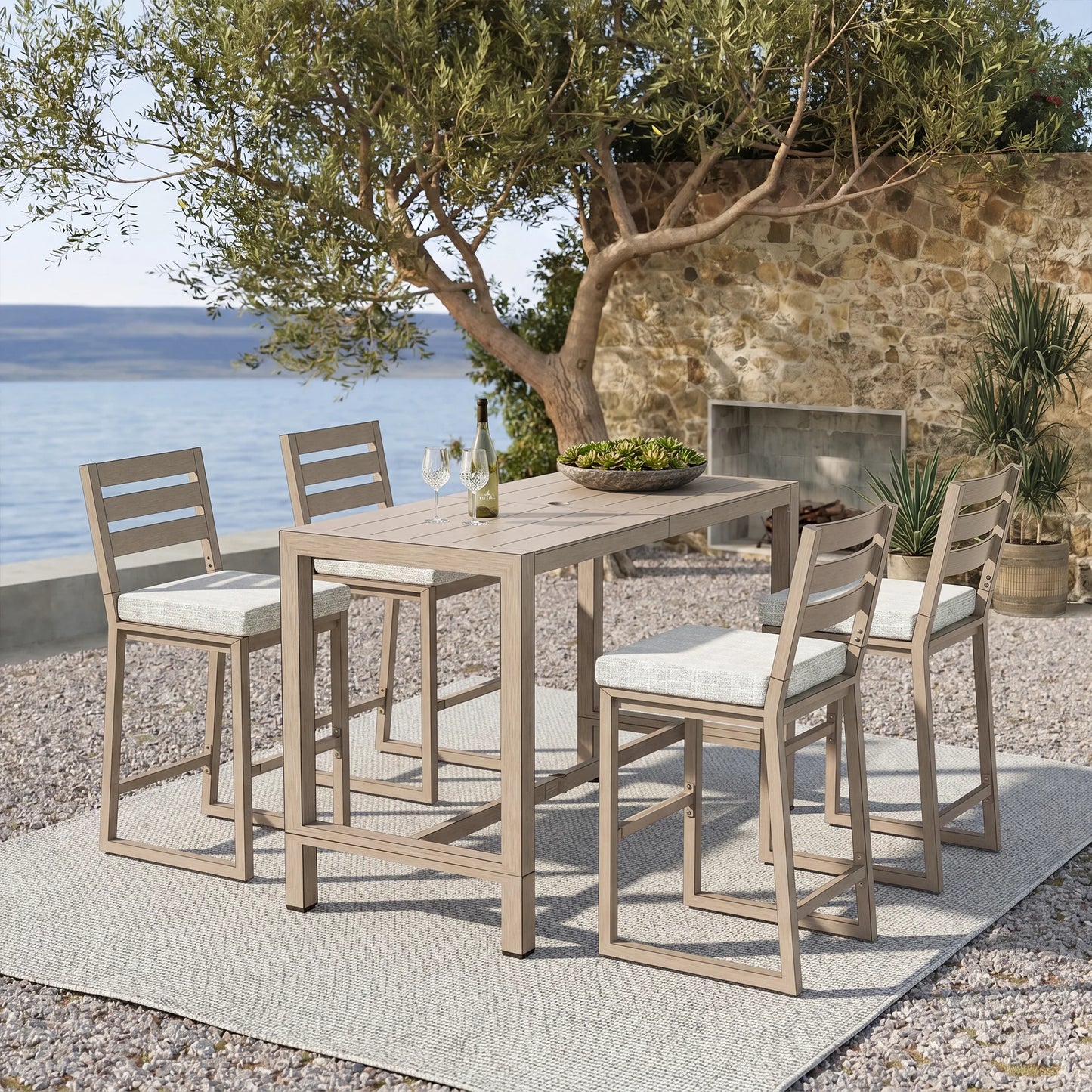 Outdoor bar set with table and chairs by a stone wall and body of water.