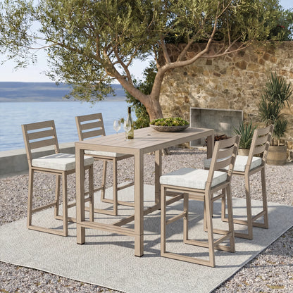 Outdoor bar set with table and chairs by a stone wall and body of water.