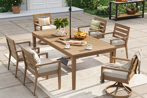 The Alcudia 7-piece aluminum outdoor dining set with a hand-brushed oak table, four classic stationary armchairs, and two swivel rockers with thick beige cushions arranged on a sunny backyard patio rug.