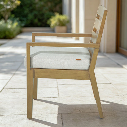 Profile side view of Alcudia aluminum outdoor dining chair with thick comfortable cushion on a stone patio.