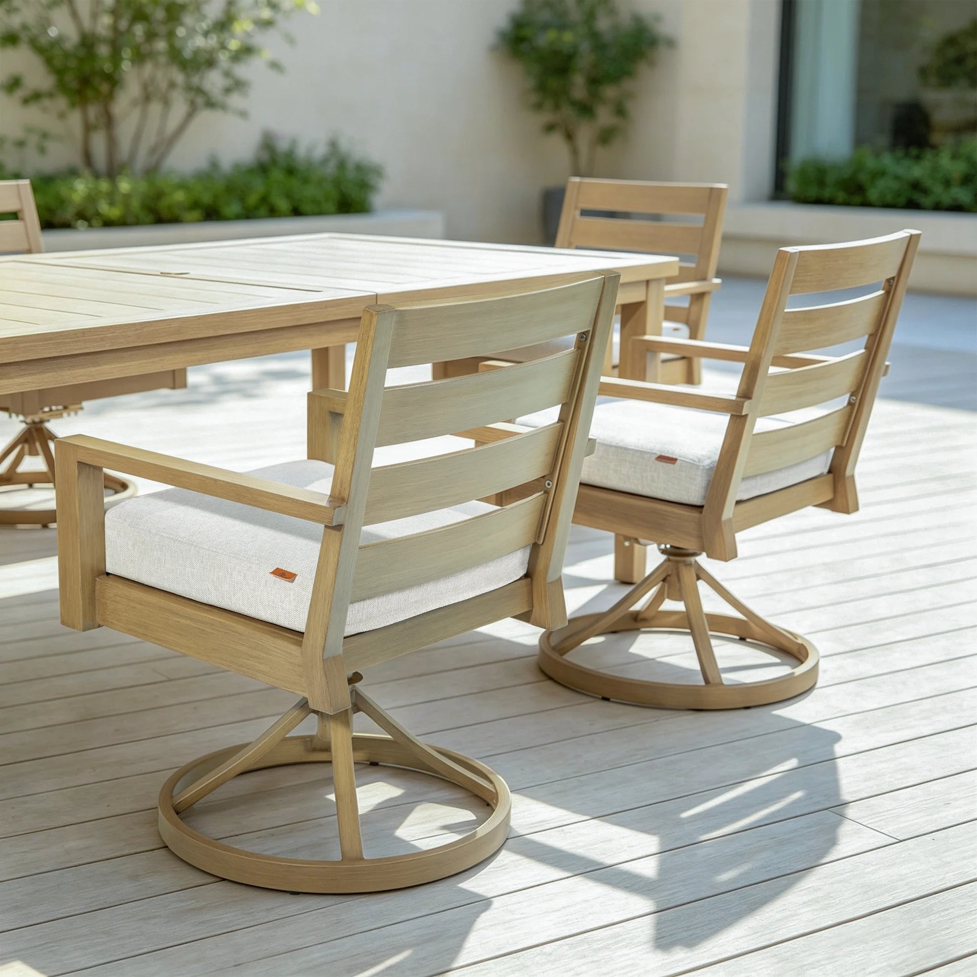 An outdoor dining arrangement featuring multiple Alcudia aluminum swivel chairs paired with a matching rectangular wood-look patio table on a wooden deck.