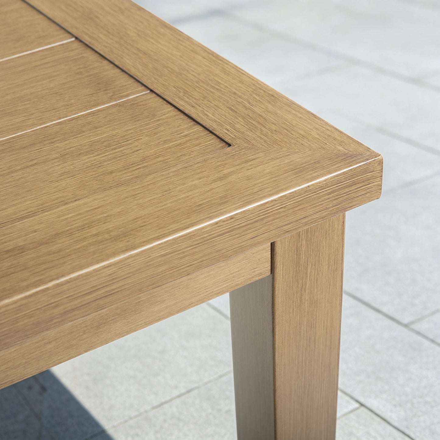 Close-up of the corner of an Alcudia aluminum patio table highlighting the intricate hand-brushed faux oak wood grain finish.