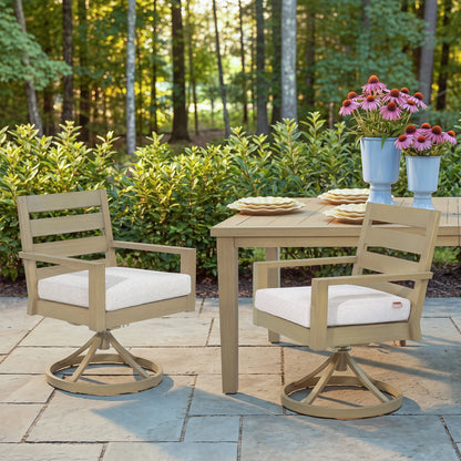 Two Alcudia outdoor swivel dining chairs styled next to a matching metal table decorated with plates and flowers on a stone paver patio.