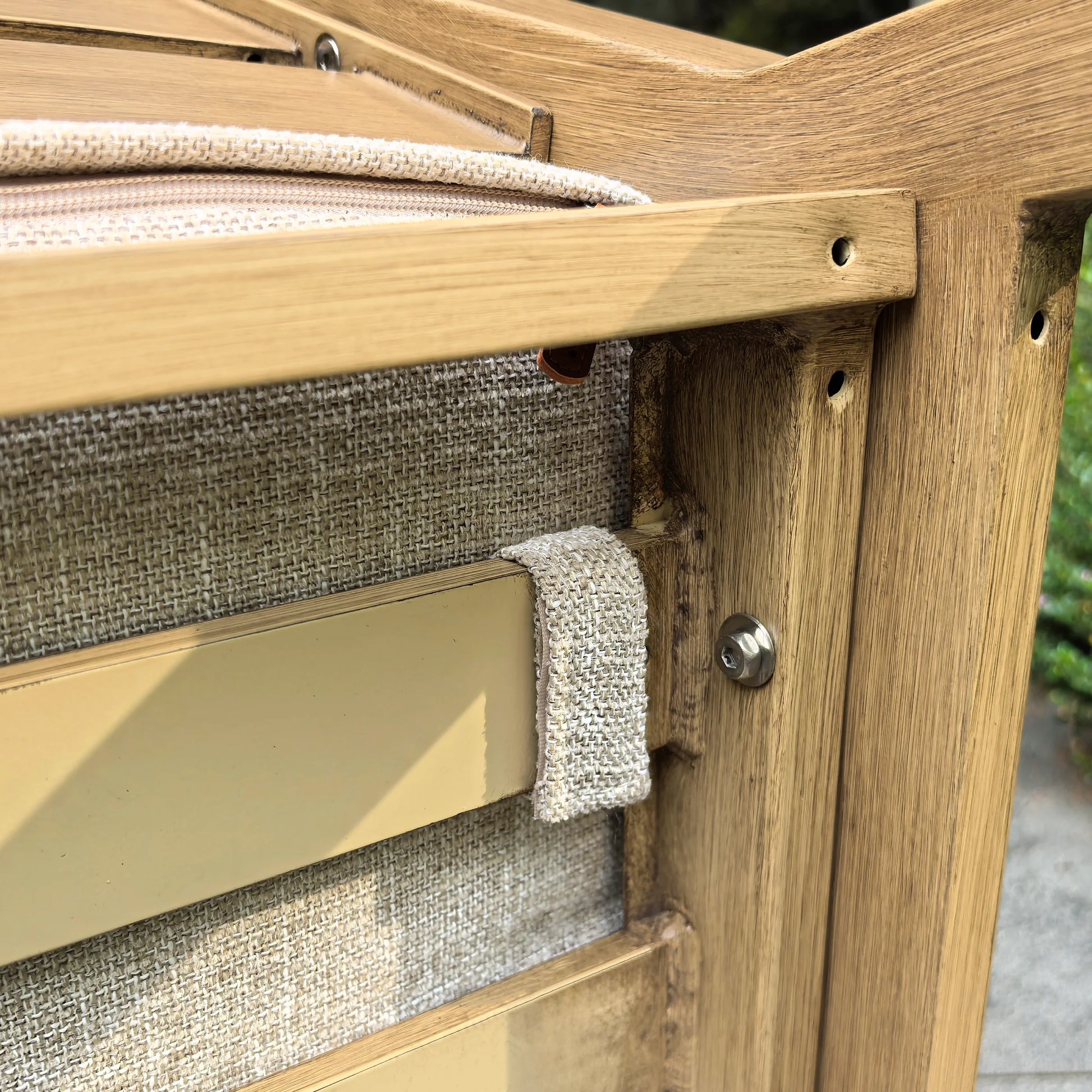 Under-seat close-up of the Alcudia patio chair showing the secure fabric fastener strap that keeps the non-slip woven cushion firmly attached to the wood-look aluminum frame.