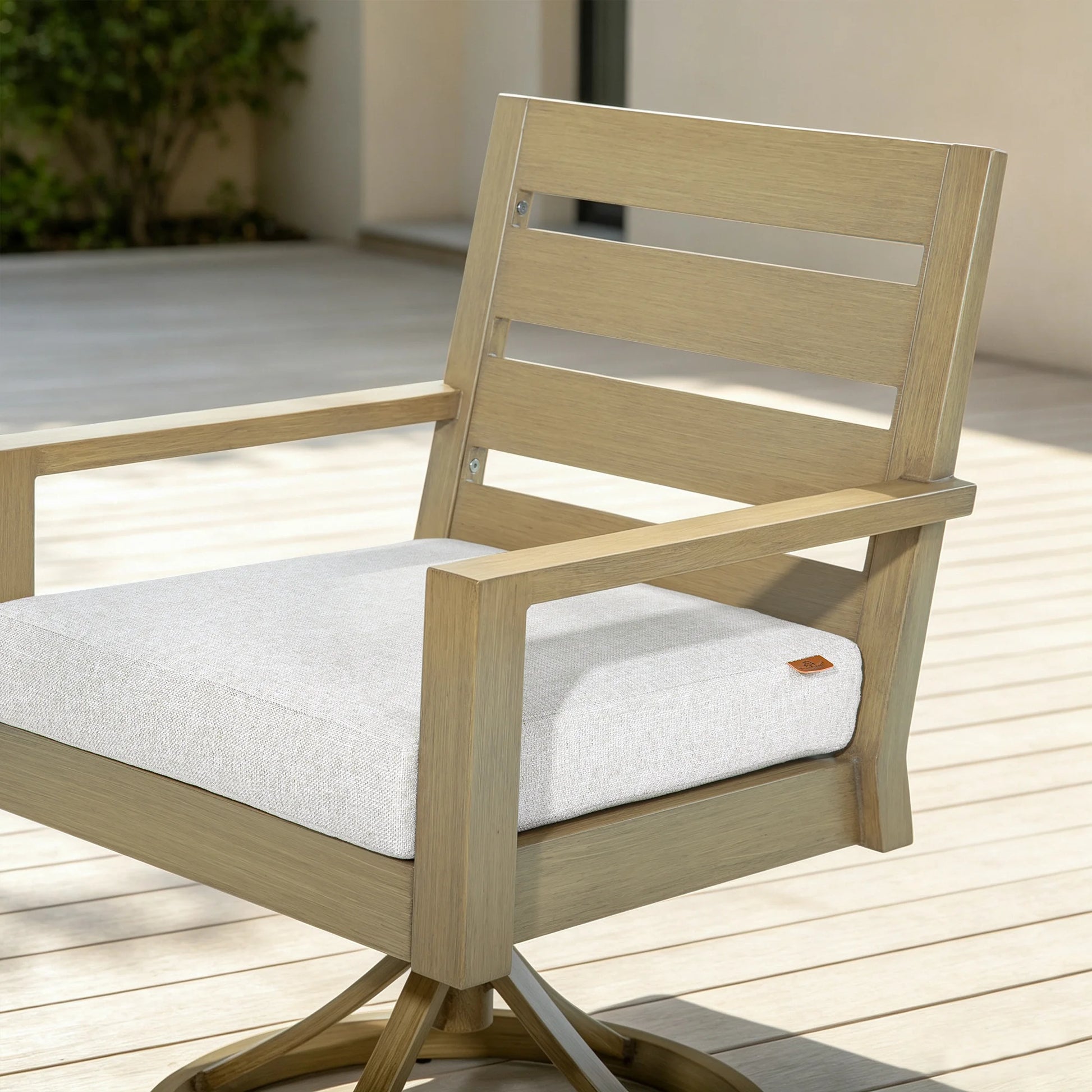 Three-quarter view of the Alcudia swivel rocker patio chair showing the 3-inch thick cream cushion and hand-brushed faux oak finish.
