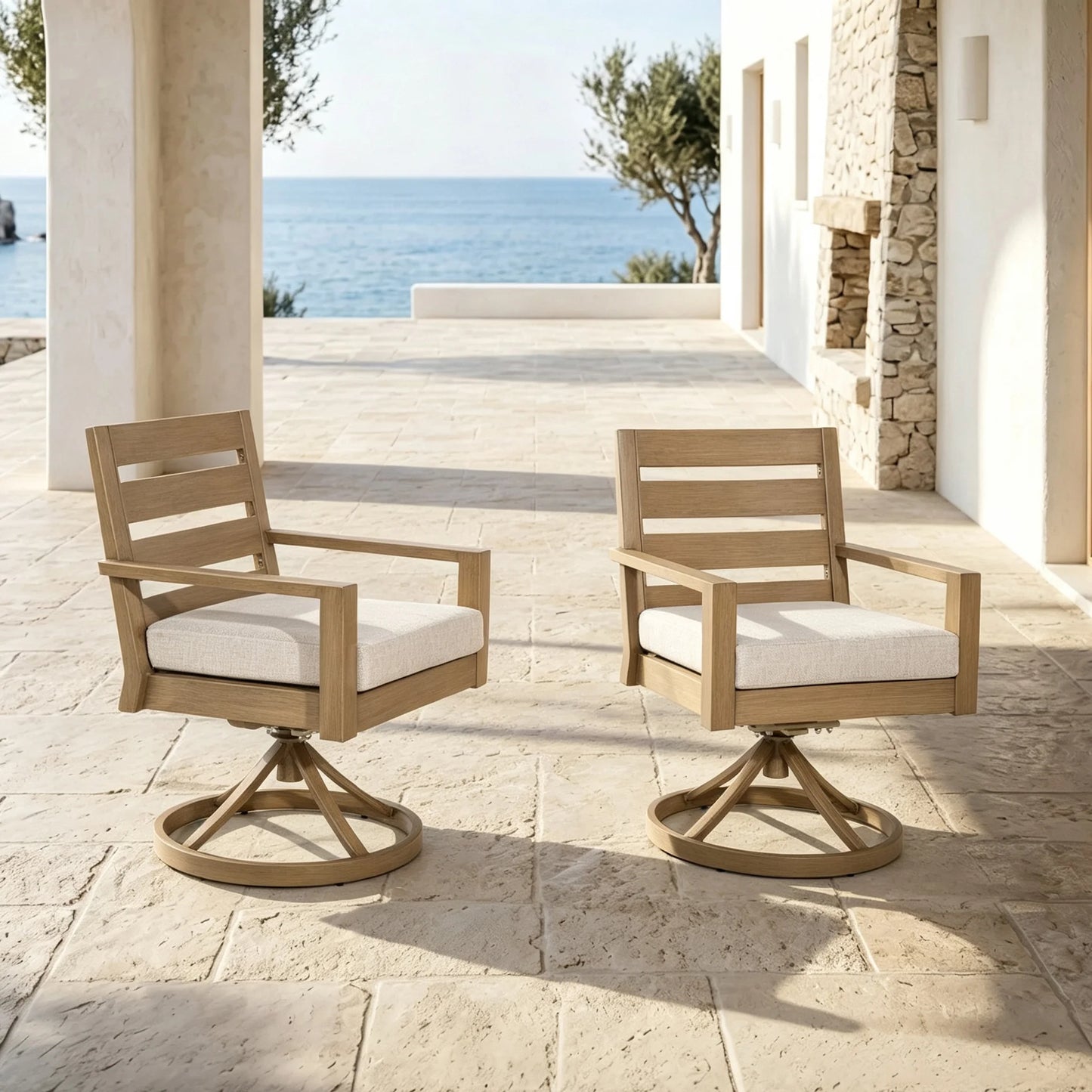 Two Alcudia 360-degree swivel rocking armchairs with textured cushions styled symmetrically on a luxury resort patio overlooking the sea.