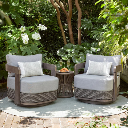 A pair of Amanarola gray outdoor swivel club chairs styled in a lush garden patio with a small round matching side table.