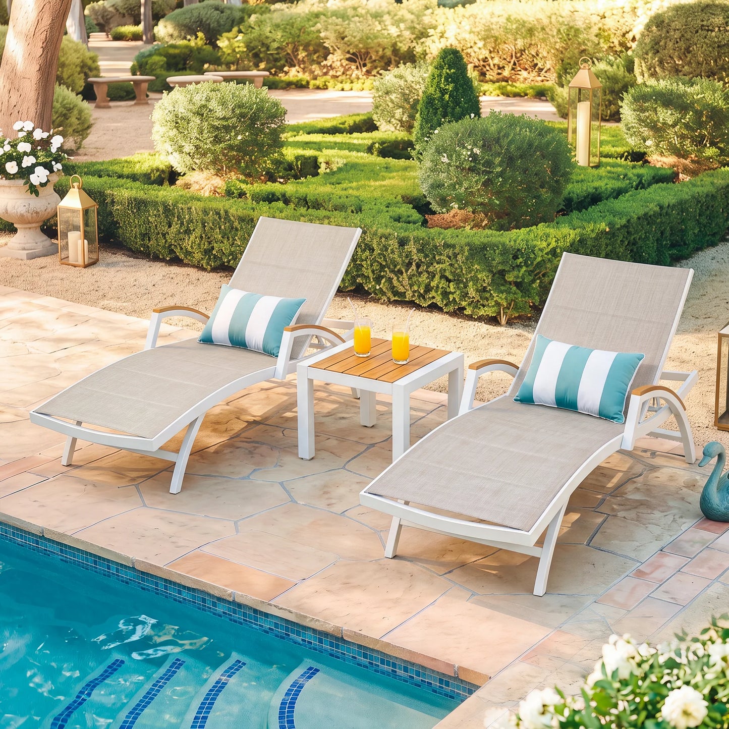High-angle view of Chambray 3-piece white aluminum pool chaise lounges with striped pillows and a side table by a sparkling blue pool.