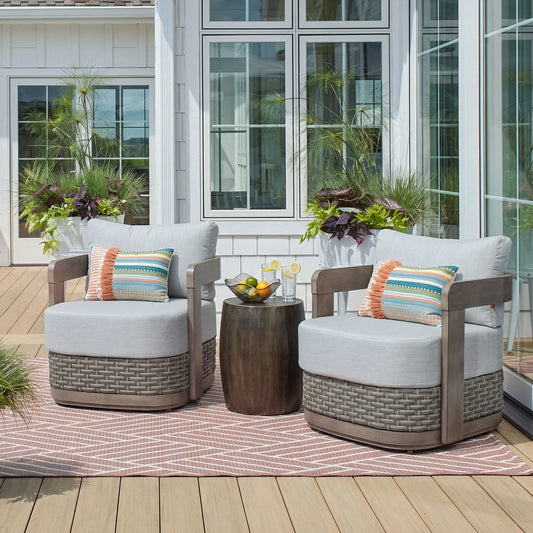 Ground-level outdoor shot of two Manarola gray fixed armchairs arranged with a round accent table on a chic patterned patio rug.
