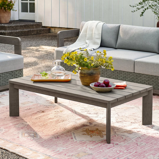 The Manarola grey rectangle aluminum outdoor coffee table styled on a pink patterned area rug in a cozy backyard setup.