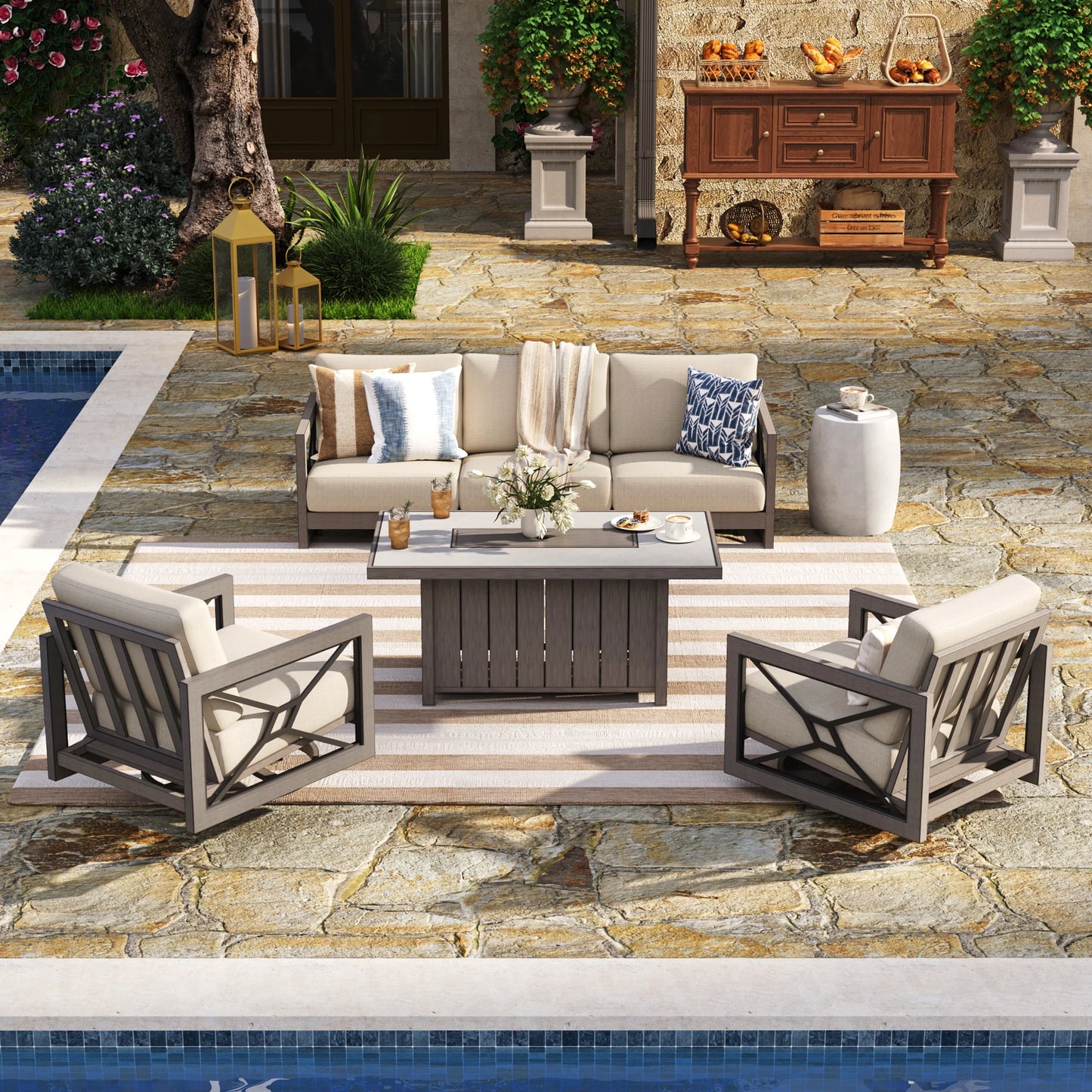 Marindo 4-piece luxury outdoor conversation set featuring a 3-seat sofa, two swivel club chairs with beige Sunbrella cushions, and a covered rectangular fire pit table on a striped rug by a resort-style pool.