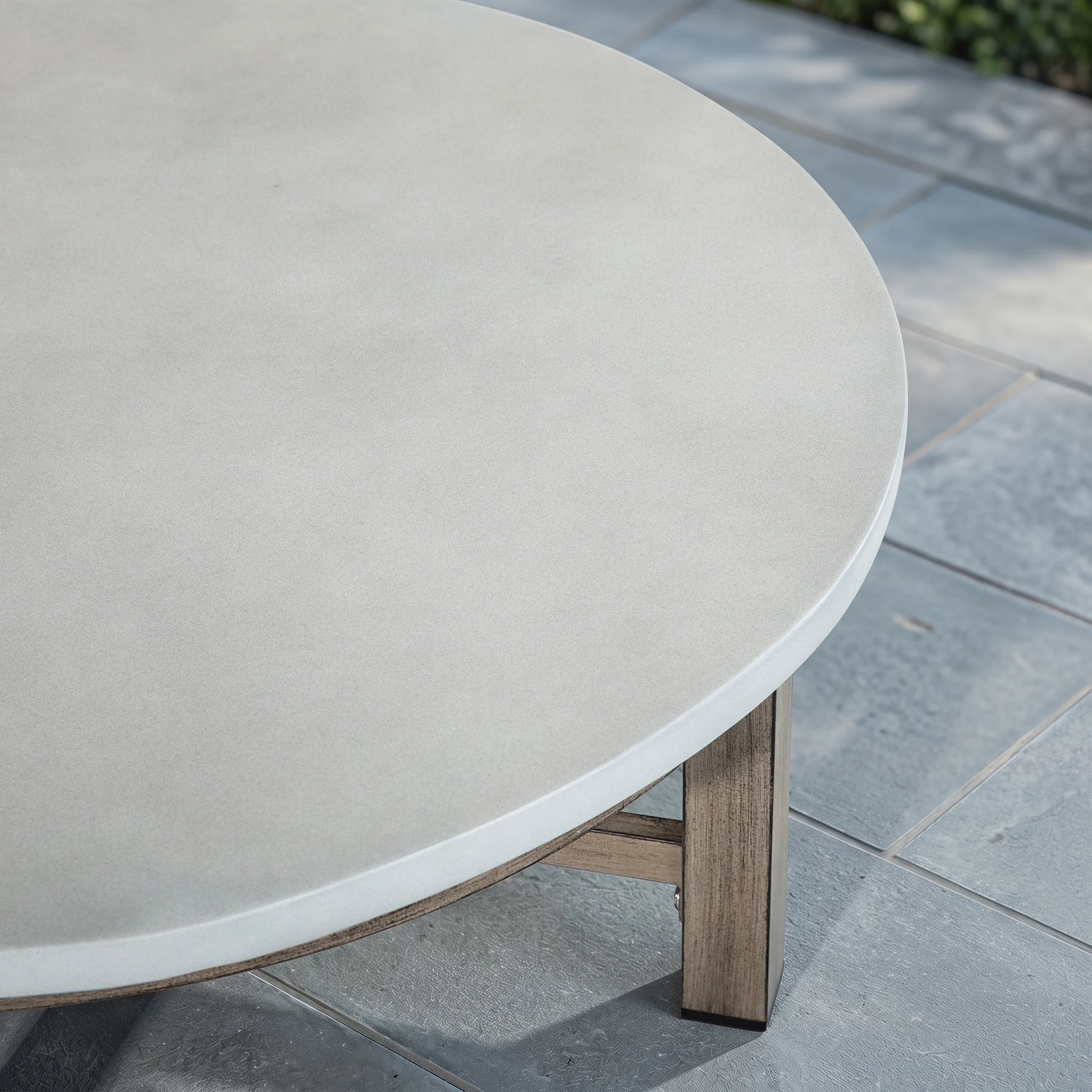Round outdoor table with a light gray top and wood-look legs on a stone patio.
