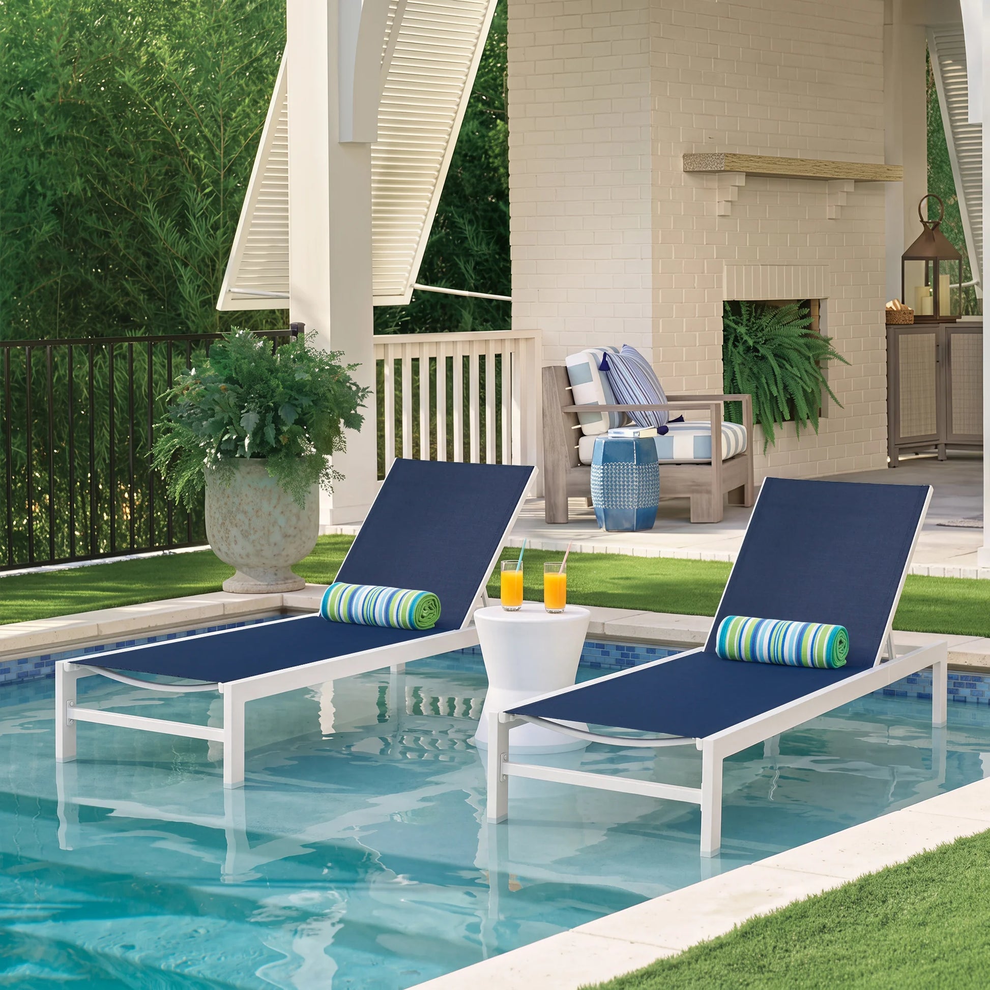 Pair of Peak Home Furnishings white aluminum in-pool chaise lounge chairs with Navy Phifertex Textilene fabric, featuring green striped bolster pillows and stainless steel hardware in a luxury swimming pool.