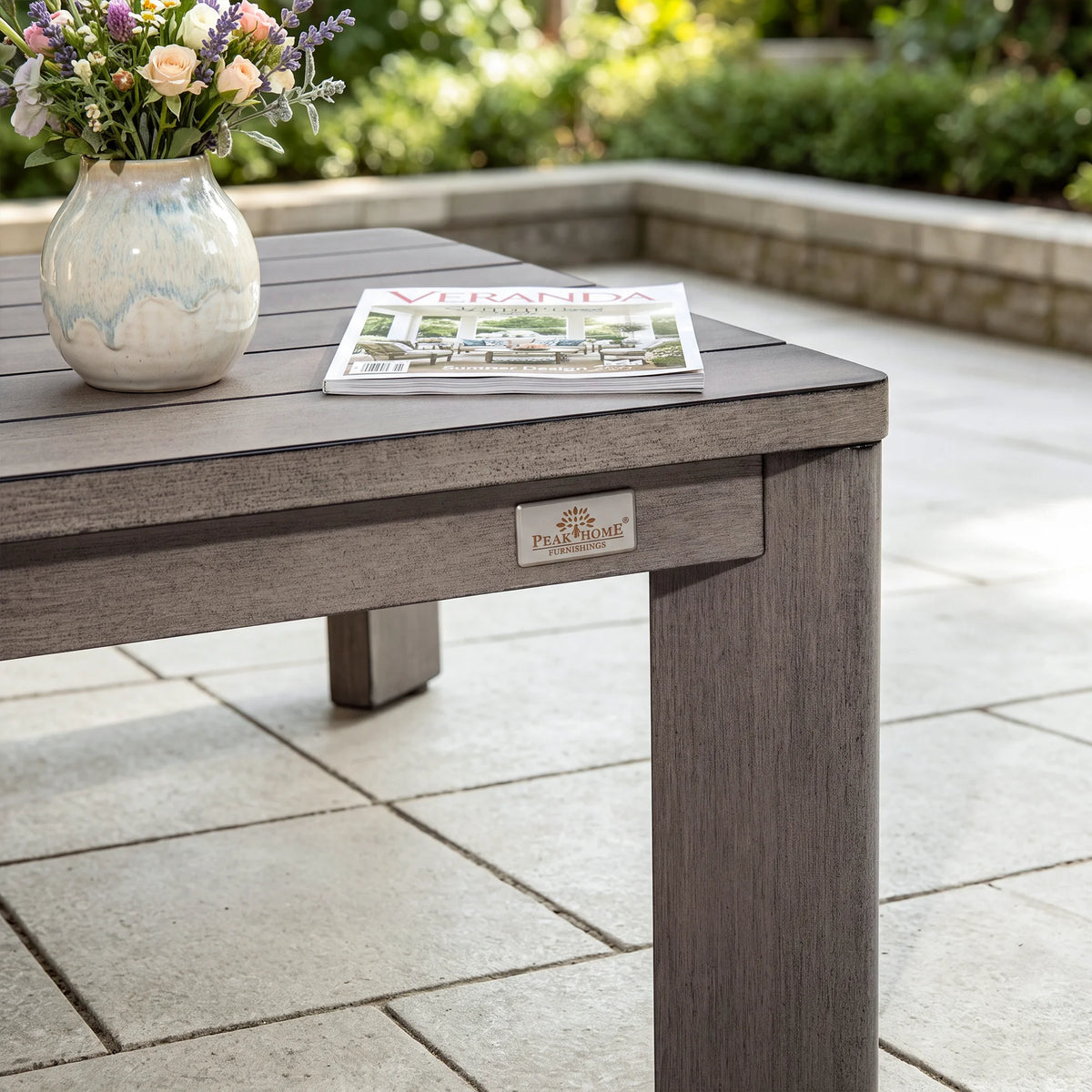 Close-up view of the Peak Home Furnishings brand metal logo plate on the side of the grey wood-look aluminum coffee table.