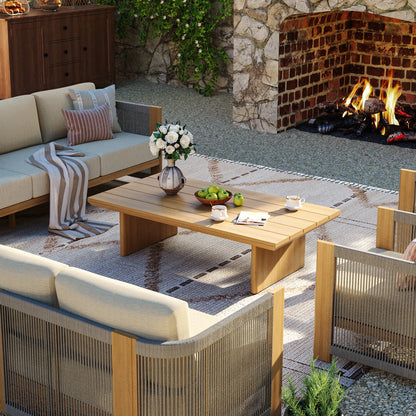 High-end backyard lounge setting featuring a rectangular aluminum cocktail table styled with apples and a white flower vase next to a stone fireplace.