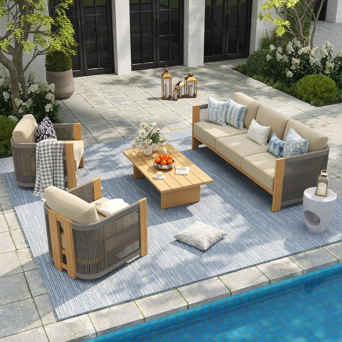 Overhead perspective of a luxury poolside patio styled with a light wood aluminum sofa set, patterned blue area rug, and casual decorative throw pillows.