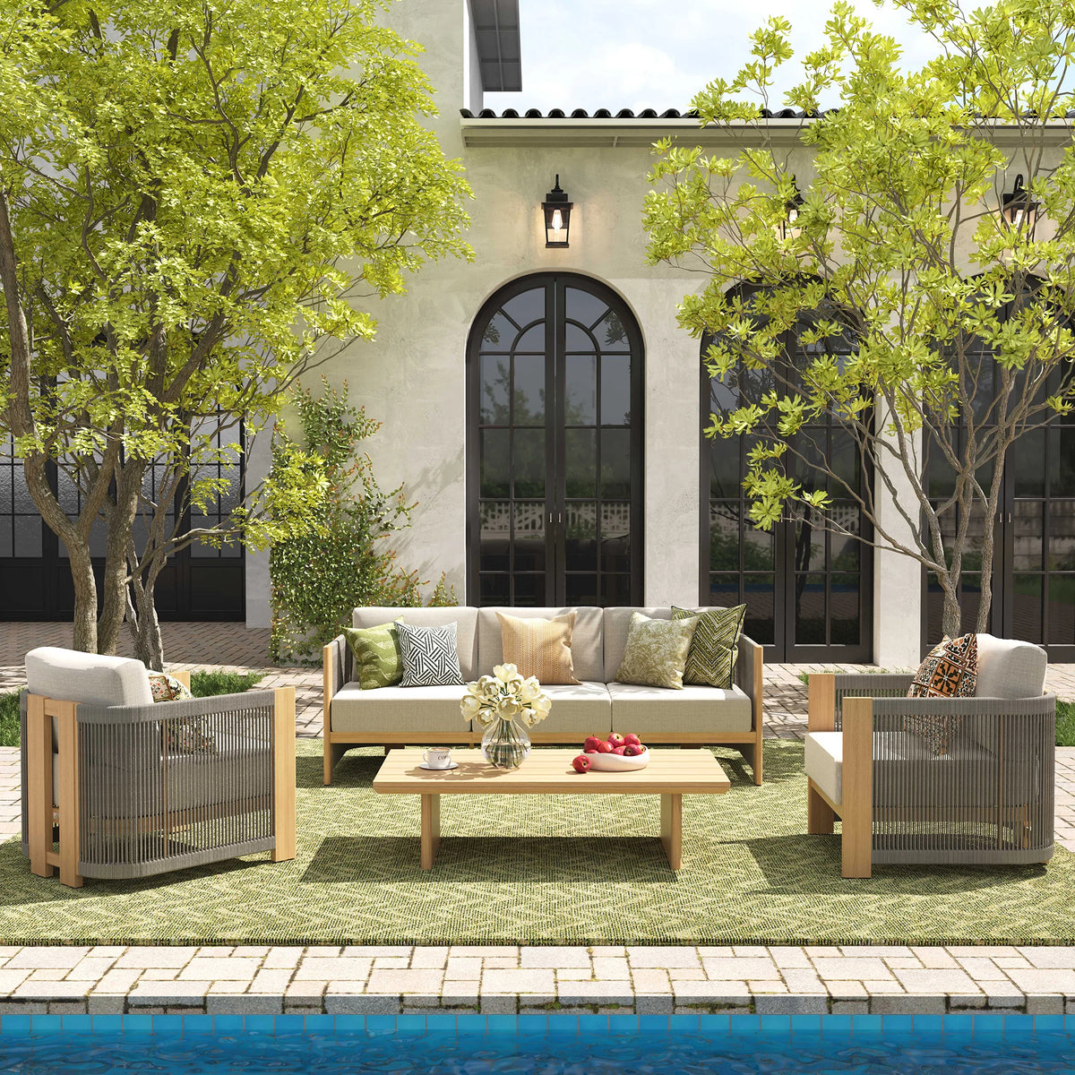 Symmetrical front view of a high-end coastal villa terrace arranged with a faux-teak aluminum sofa and club chair combination over a sage green woven outdoor rug.