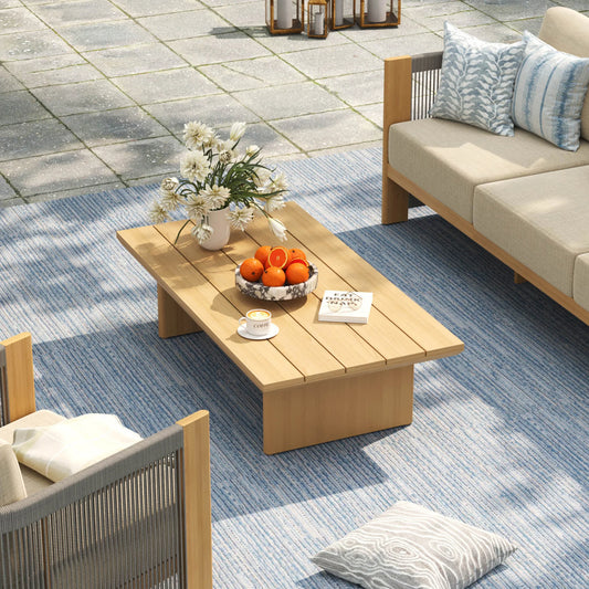 Top-down angled shot of a durable slatted-top patio cocktail table adorned with fresh oranges on a textured blue geometric rug.